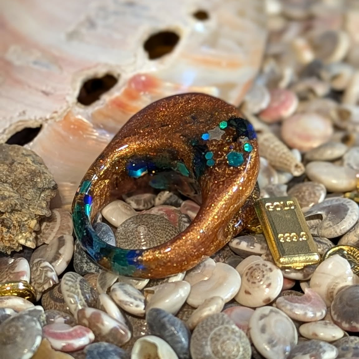 Gold ring with blue gemstones on a bed of seashells and small stones