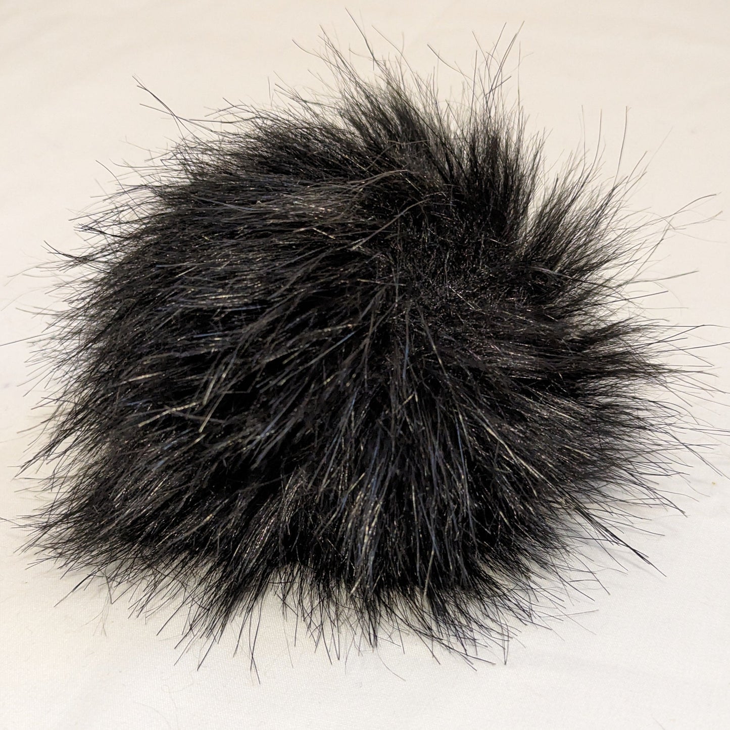 A collection of faux fur pompoms in various colors including beige, gray, pink, black, and white.